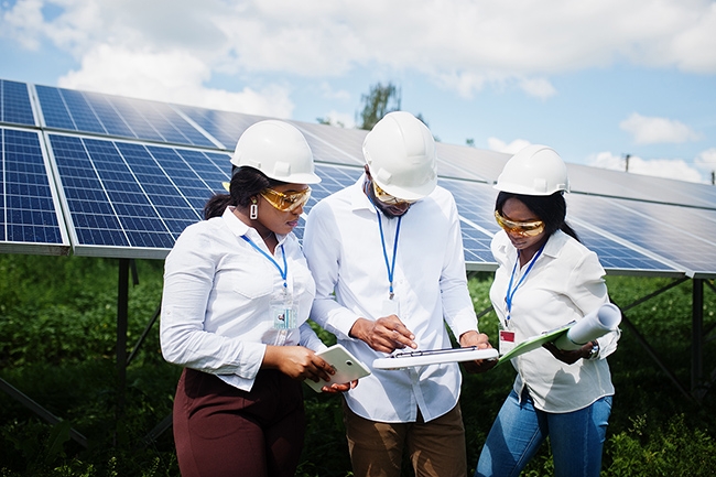 Diverse construction crew examining plans near field of solar panels