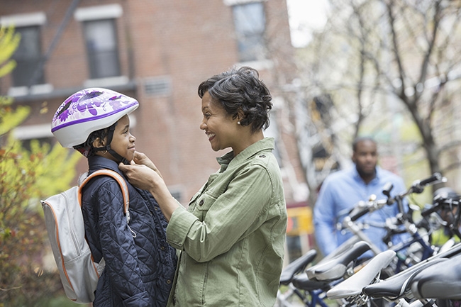 Mom helping young daughter with bike helmet