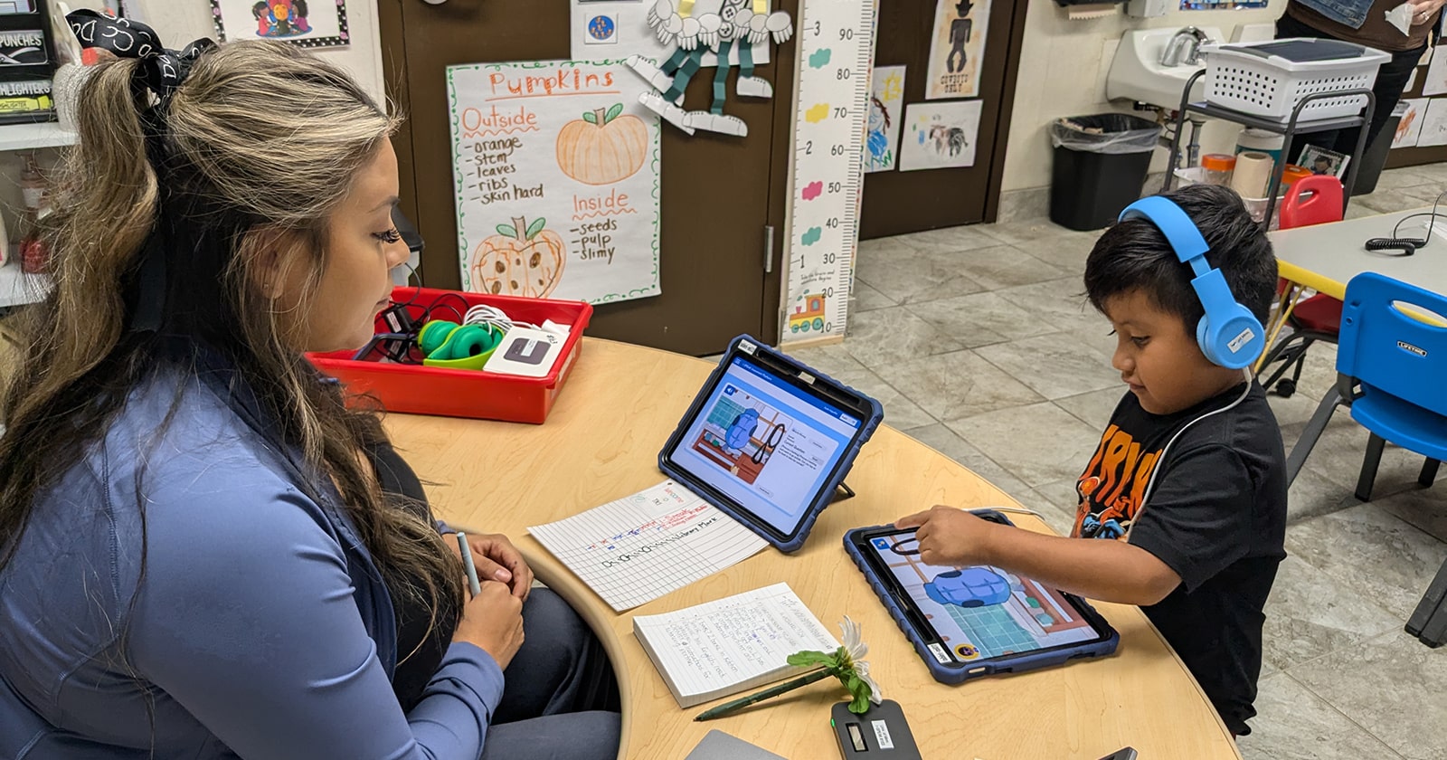 A teacher supervises a Pre-K student using a tablet in the classroom