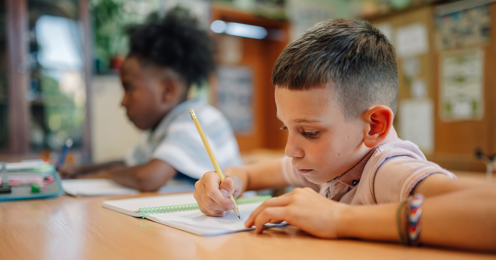 Two first grade boys write in a workbook with pencils 