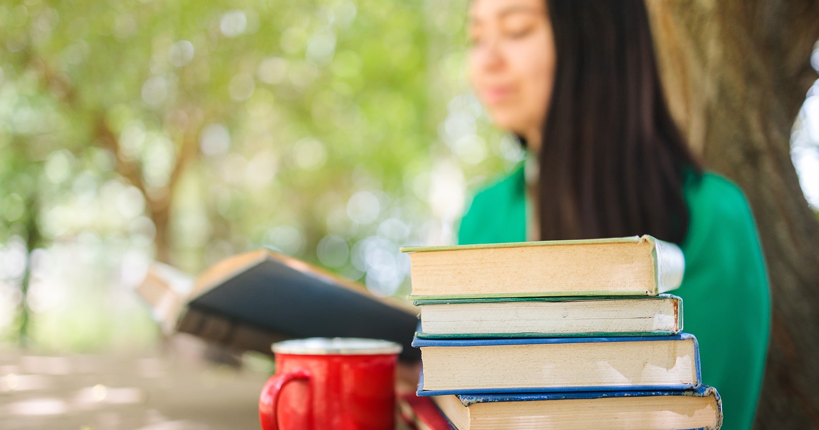 College student shown studying outside, a stack of books and coffee mug in the foreground