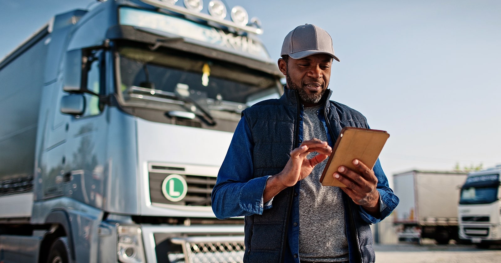 A truck driver checks information on a tablet while standing near his 18-wheeler