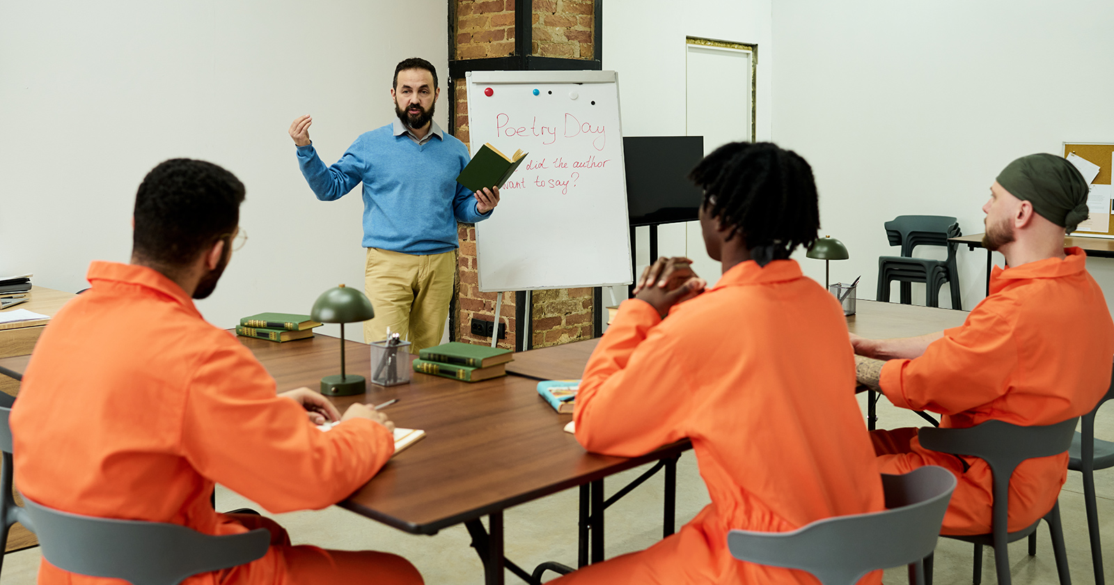 Man teaching poetry class to group of young adult men in orange prison uniforms