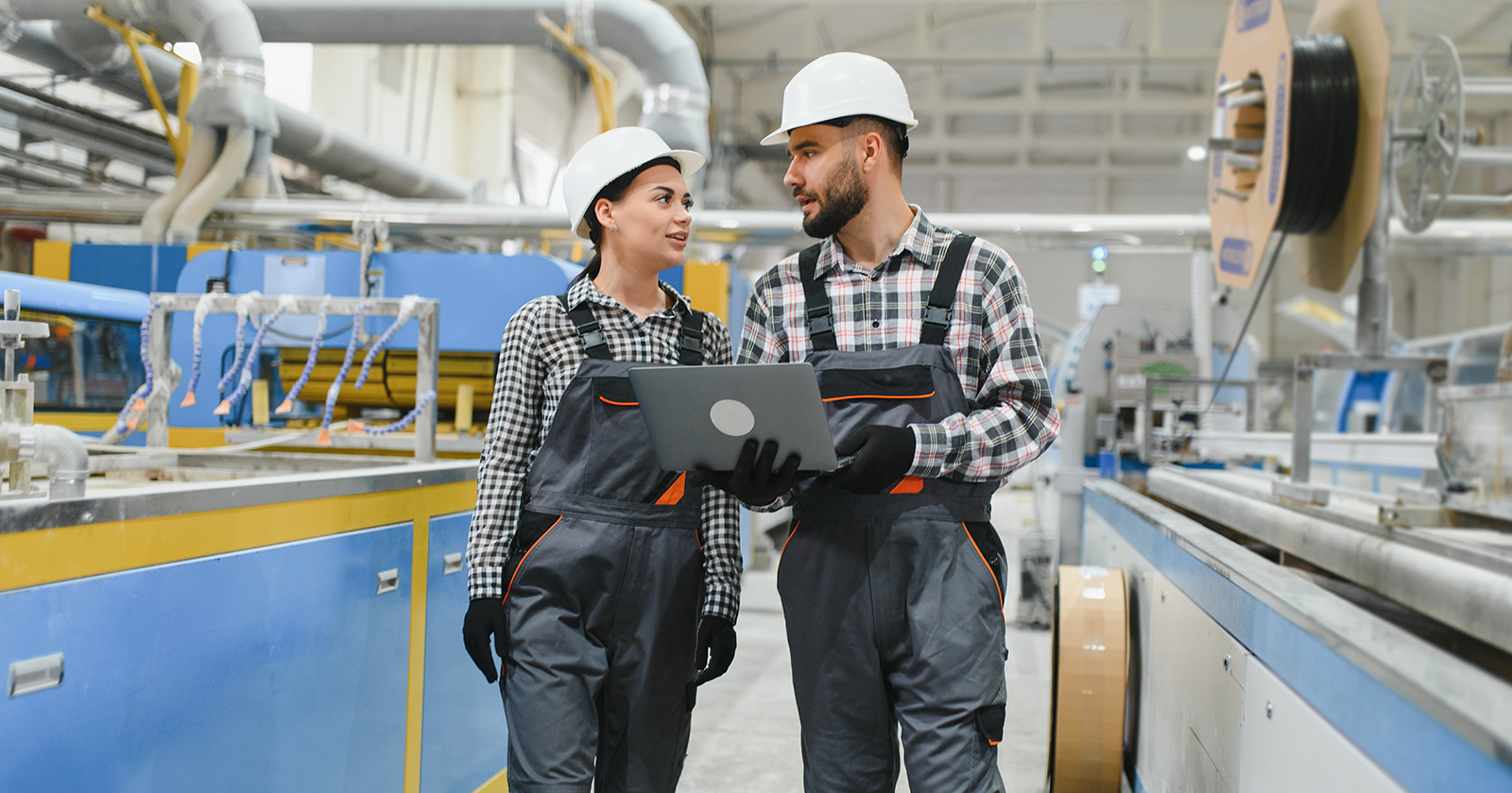 Two trainees in a warehouse wearing hard hats and overalls