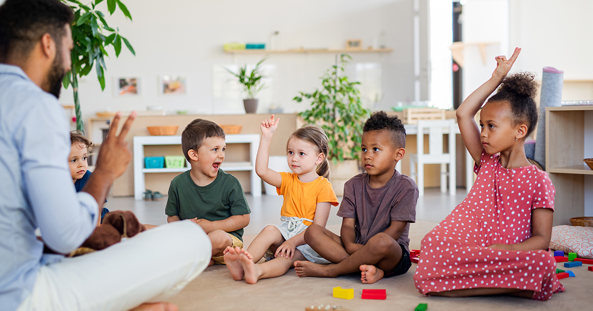 a teacher is sitting with kindergarten in a circle on a floor