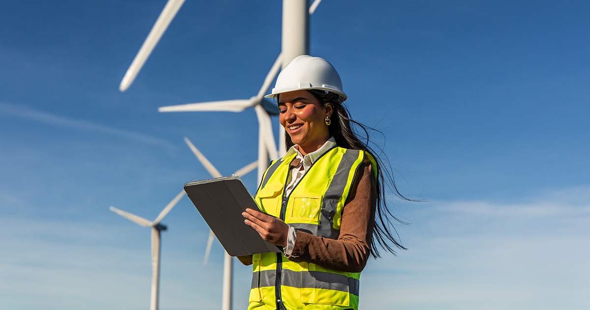 female student engineer using tablet in wind turbine power plant generating green energy