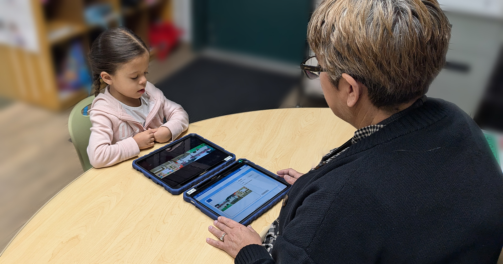 A Pre-K student uses a tablet as an educator guides her during an assessment in a classroom