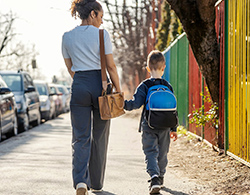 Mother and young son shown from behind walking to school