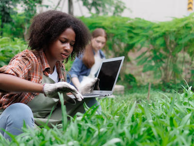 Two high school students in a garden, checking information on a laptop