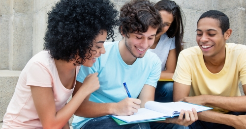 Diverse group of students sitting outside, conferring over an open book