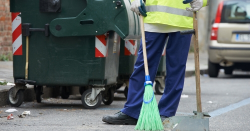 Sanitation worker with broom near trash can