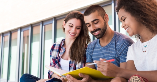 Three college students smiling down at a notebook