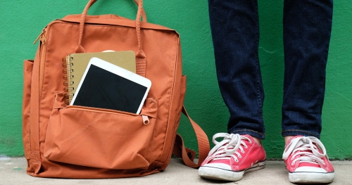 Close-up of backpack against a green wall and a student standing next to it