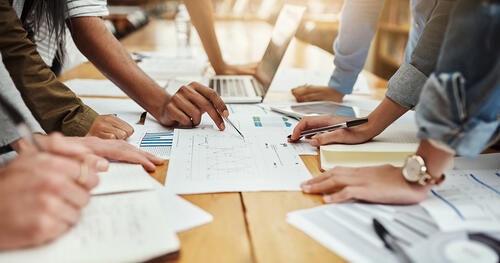 Colleagues lean over a table to view data on sheets of paper