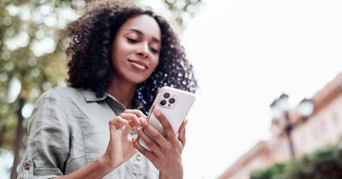 College-age Black woman looking down at her phone outside