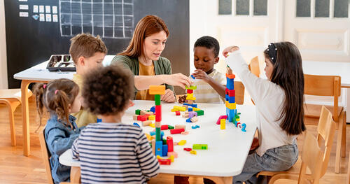 Pre-K instructor assists diverse group of children who are playing with colorful blocks in a classroom