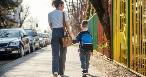 Mother and young son shown from behind walking to school