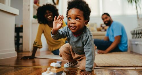 Smiling parents watch as their infant son crawls on the floor