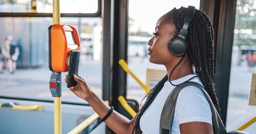 College student wearing headphones taps her phone to pay for a bus ride