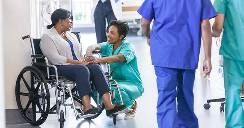 A hospital nurse crouches down to talk with a patient in a wheelchair