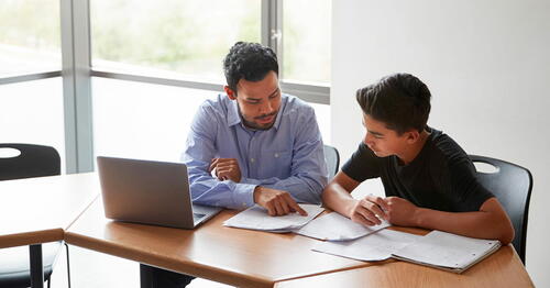 A tutor helps a teen boy with a workbook assignment
