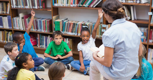 kids sitting on a floor in library and listening the teacher