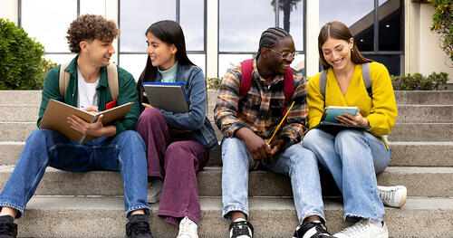 group of four students are sitting on the stairs ourside of college building