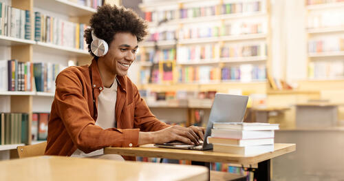 young men smiling while looking at laptop in library