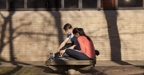 Two college students studying on a campus bench 