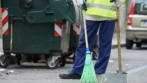 Sanitation worker with broom near trash can
