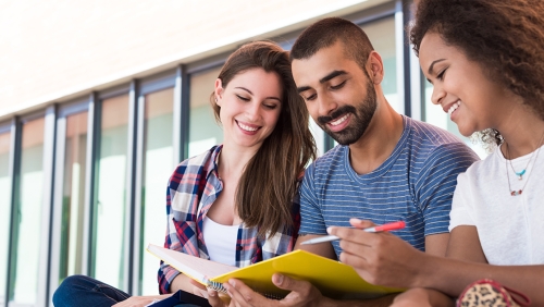 Three college students smiling down at a notebook