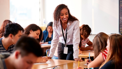 High school teacher leaning over a desk and speaking to students
