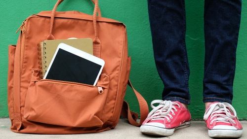 Close-up of backpack against a green wall and a student standing next to it