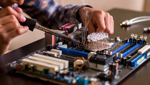 Hands working on a circuit board with tools