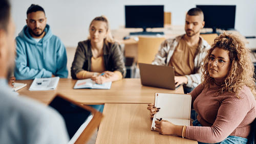 Diverse group of college students sitting at a table focus on an instructor in the foreground