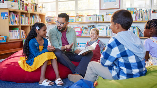 a male teacher is sitting on a floor in circle with kids