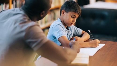 A man helps a schoolchild with a worksheet