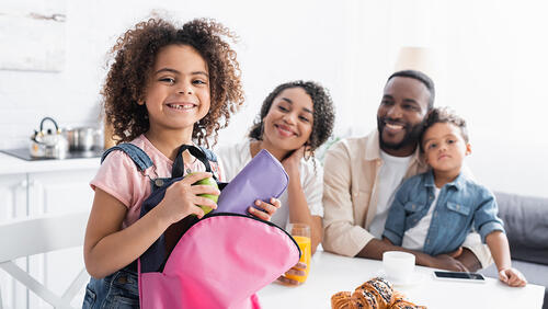 a kid is packing a bag for school after breakfast with her family