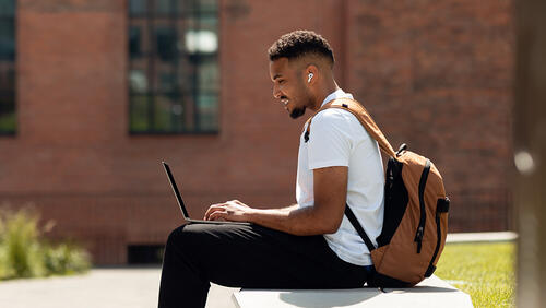 a young men sitting on a banch with a laptop