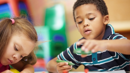 Two preschool-aged children play with crayons
