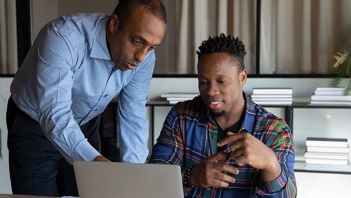 Mentor points to something on a computer screen as young Black intern looks