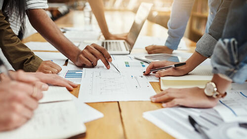Colleagues lean over a table to view data on sheets of paper