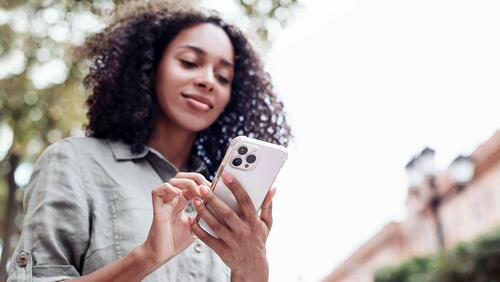 College-age Black woman looking down at her phone outside