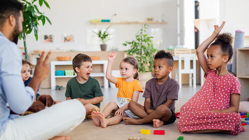 Pre-K instructor sits on the floor of his classroom with a small group of students
