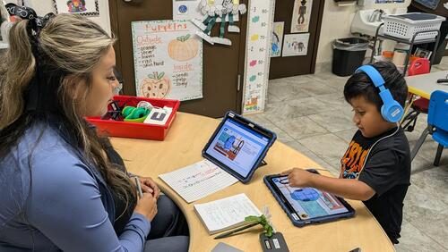 A teacher supervises a Pre-K student using a tablet in the classroom