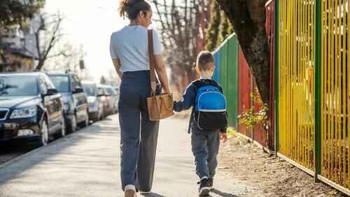 Mother and young son shown from behind walking to school