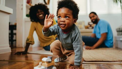 Smiling parents watch as their infant son crawls on the floor