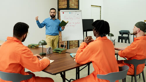 Man teaching poetry class to group of young adult men in orange prison uniforms