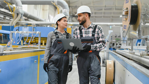 Two trainees in a warehouse wearing hard hats and overalls
