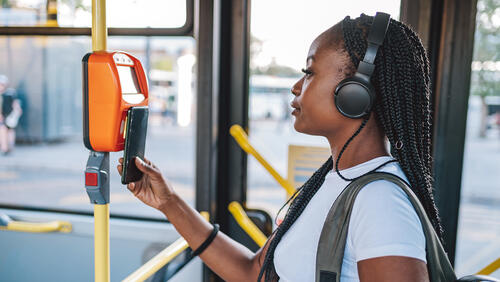 College student wearing headphones taps her phone to pay for a bus ride
